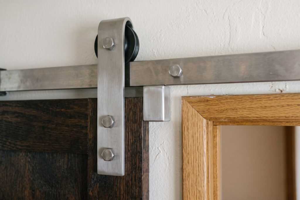 Close-up of a modern sliding door track and hardware featuring a sleek metal finish and a rustic wooden door.